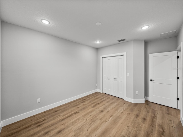 unfurnished bedroom with a textured ceiling, visible vents, baseboards, light wood-style floors, and a closet