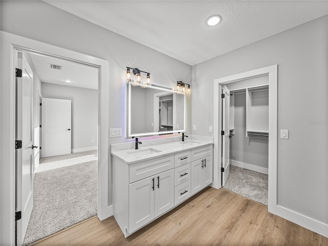 full bath featuring wood finished floors, visible vents, a sink, double vanity, and a walk in closet