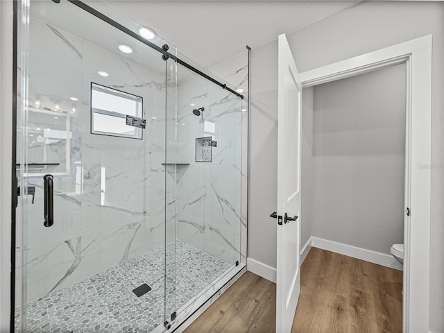 full bath featuring a marble finish shower, wood finished floors, toilet, and baseboards