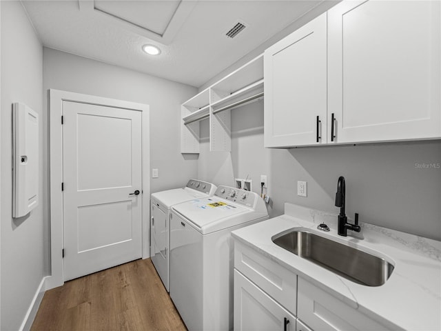 washroom featuring cabinet space, visible vents, washer and dryer, light wood-style floors, and a sink