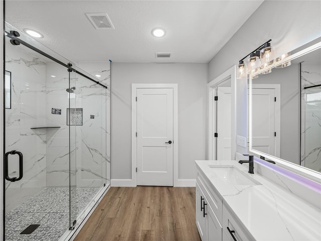 full bathroom with a marble finish shower, vanity, wood finished floors, and visible vents