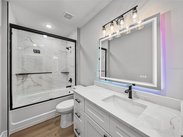 bathroom featuring visible vents, toilet, wood finished floors, combined bath / shower with glass door, and vanity