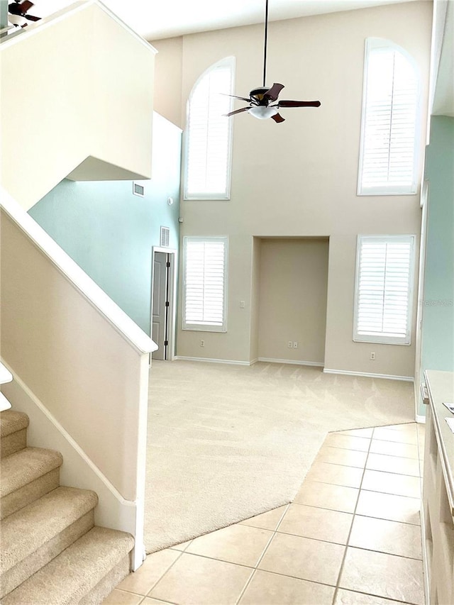 interior space with ceiling fan, stairs, a towering ceiling, light carpet, and light tile patterned flooring