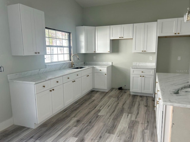 kitchen featuring light stone counters, white cabinetry, a sink, and light wood-style flooring