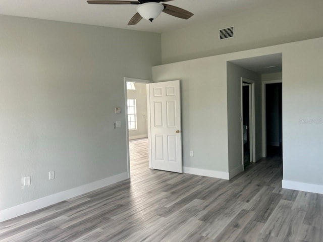 empty room with a ceiling fan, baseboards, visible vents, and wood finished floors