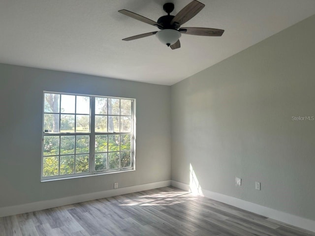 spare room featuring light wood-type flooring, a ceiling fan, and baseboards