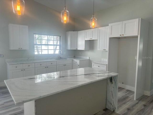 kitchen featuring light stone counters, pendant lighting, white cabinets, a kitchen island, and a sink