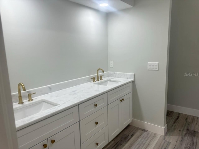 bathroom with wood finished floors, a sink, baseboards, and double vanity