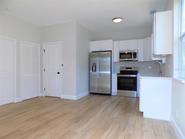 kitchen with stainless steel appliances, light countertops, visible vents, light wood-style floors, and white cabinetry