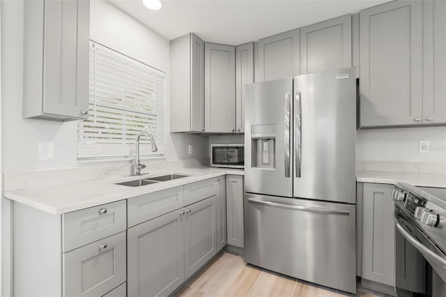 kitchen with light wood finished floors, stainless steel appliances, gray cabinetry, a sink, and light stone countertops