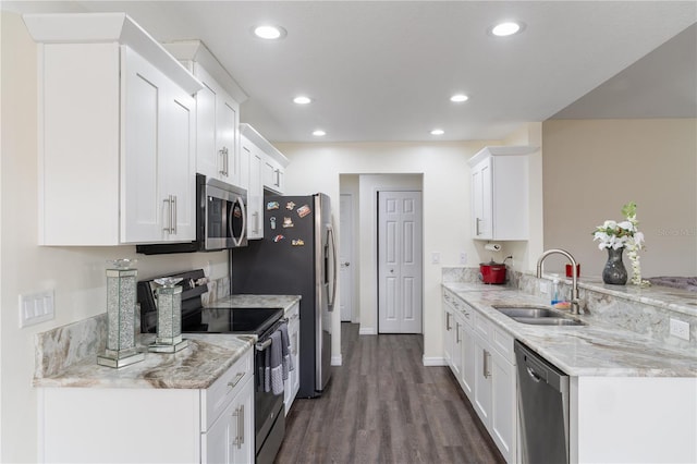 kitchen with appliances with stainless steel finishes, a peninsula, light stone countertops, white cabinetry, and a sink