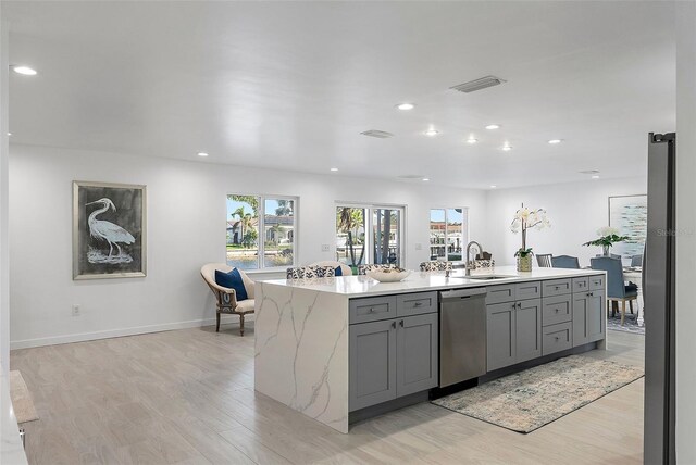 1984 Kansas Ave NE, Saint Petersburg, FL 33703 - kitchen featuring gray cabinets, stainless steel dishwasher, a sink, an island with sink, and light stone countertops