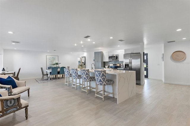 1984 Kansas Ave NE, Saint Petersburg, FL 33703 - kitchen featuring white cabinets, decorative backsplash, appliances with stainless steel finishes, a kitchen breakfast bar, and light stone counters