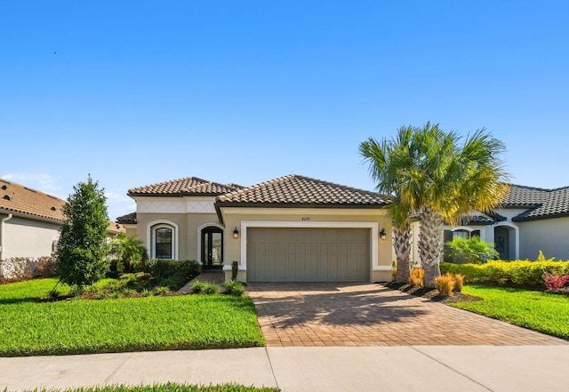 mediterranean / spanish house featuring a garage, a tiled roof, decorative driveway, stucco siding, and a front yard