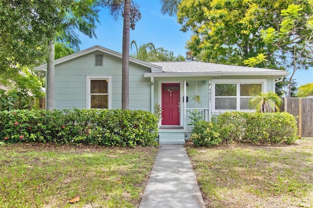 bungalow-style house with entry steps, roof with shingles, a front yard, and fence