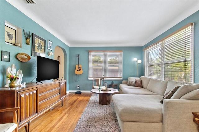 living area featuring arched walkways, plenty of natural light, wood finished floors, and baseboards