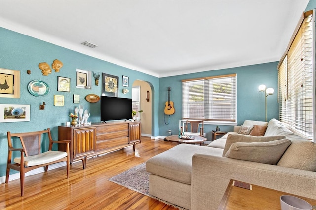 living area with arched walkways, wood finished floors, visible vents, and baseboards