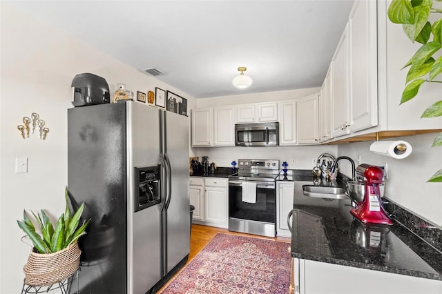 kitchen with visible vents, appliances with stainless steel finishes, white cabinetry, a sink, and dark stone countertops