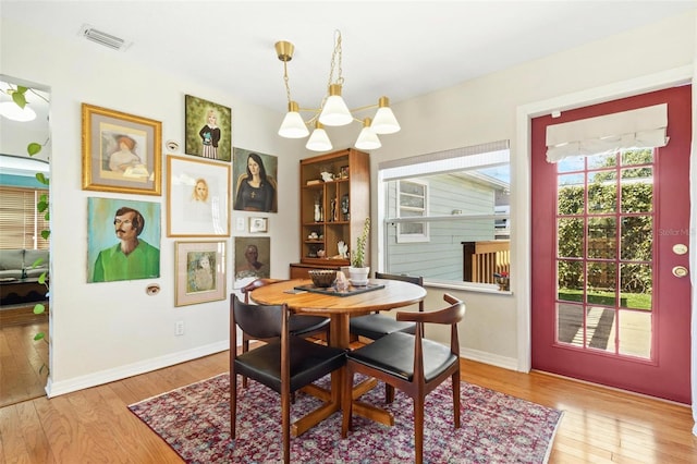 dining space with baseboards, light wood-style flooring, visible vents, and an inviting chandelier