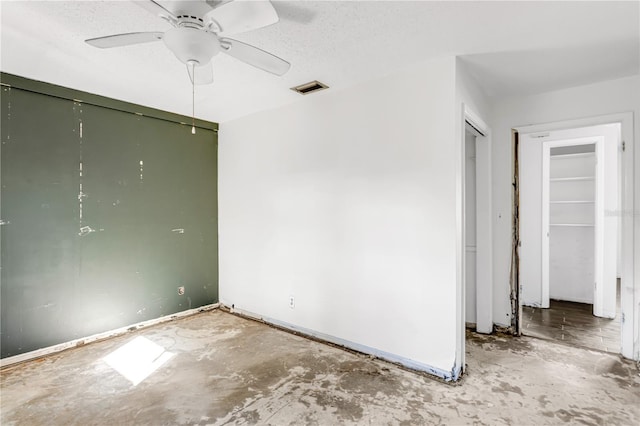 spare room featuring a textured ceiling, concrete floors, visible vents, baseboards, and a ceiling fan