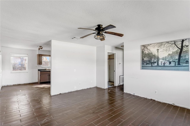 unfurnished living room featuring dark wood-style floors, a ceiling fan, visible vents, and a textured ceiling