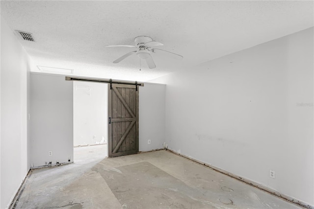 unfurnished room with a barn door, visible vents, ceiling fan, and a textured ceiling