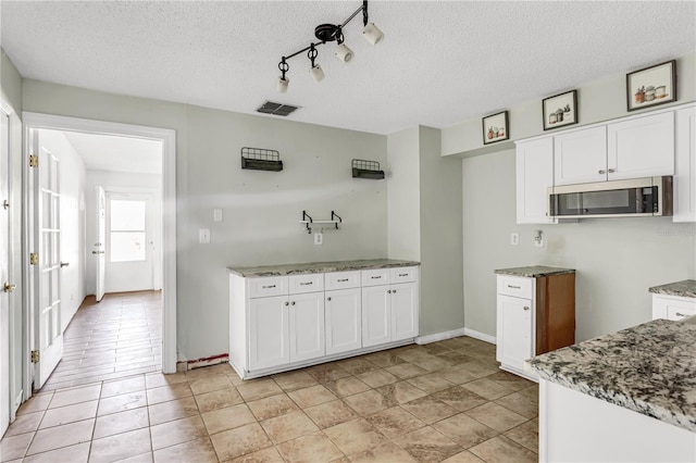 kitchen with stainless steel microwave, visible vents, white cabinets, a textured ceiling, and light stone countertops