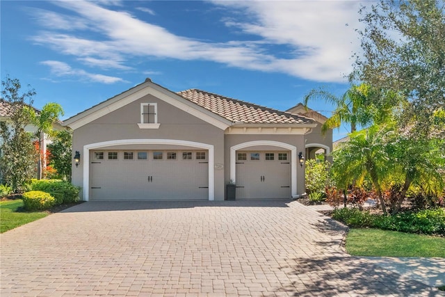 view of front facade featuring a garage, decorative driveway, a tiled roof, and stucco siding