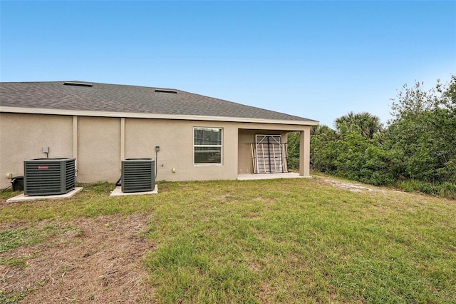 back of house with central AC, a shingled roof, a lawn, and stucco siding