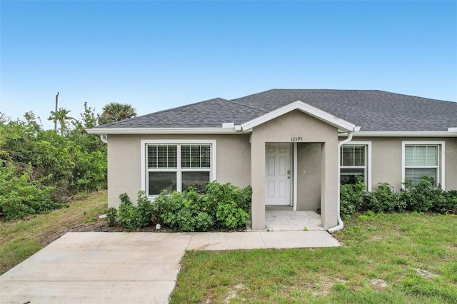 view of front of house featuring roof with shingles, a front yard, and stucco siding