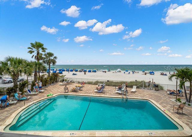 community pool featuring a view of the beach, a water view, fence, and a patio