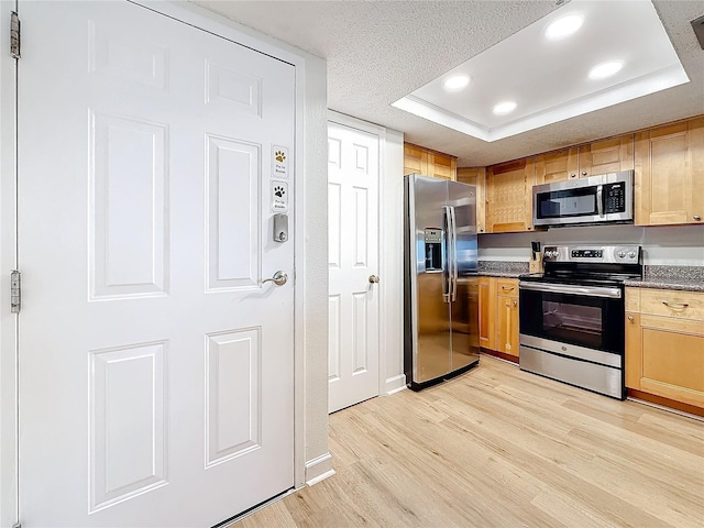 kitchen featuring a textured ceiling, appliances with stainless steel finishes, light wood-type flooring, dark countertops, and a raised ceiling