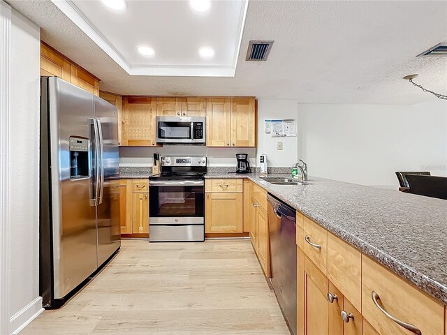 kitchen featuring visible vents, appliances with stainless steel finishes, a tray ceiling, light wood-style floors, and a sink