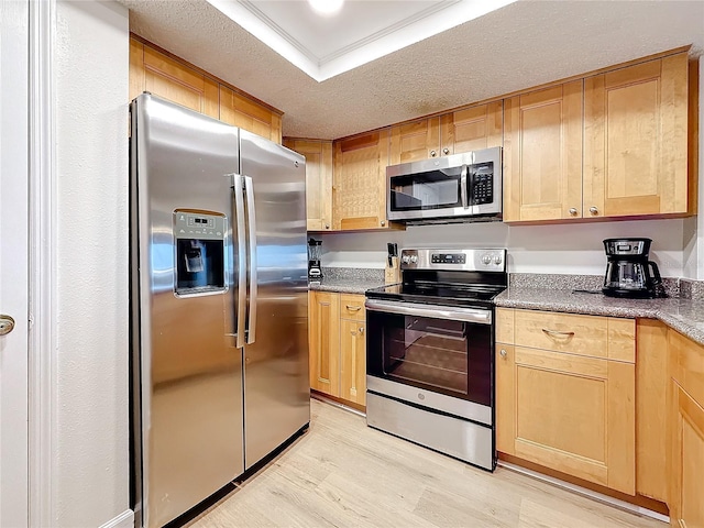 kitchen with dark countertops, a raised ceiling, appliances with stainless steel finishes, a textured ceiling, and light wood-type flooring