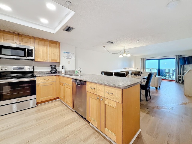 kitchen with light wood finished floors, visible vents, appliances with stainless steel finishes, a sink, and a peninsula