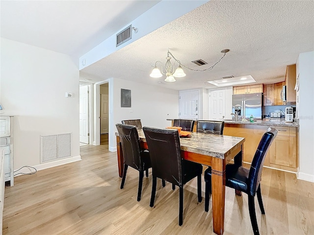 dining area featuring baseboards, light wood-style flooring, visible vents, and a textured ceiling