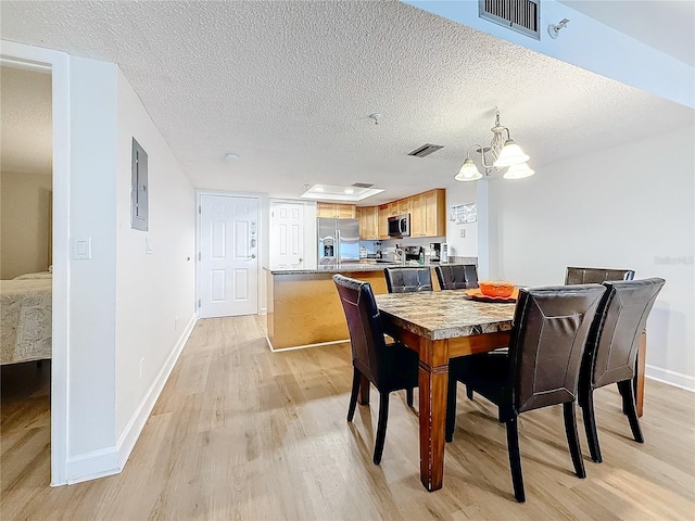 dining room featuring a textured ceiling, light wood-type flooring, visible vents, and baseboards