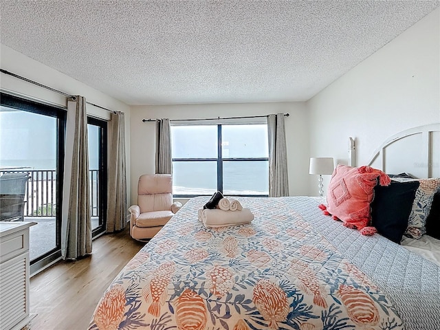 bedroom with access to outside, light wood-style flooring, and a textured ceiling