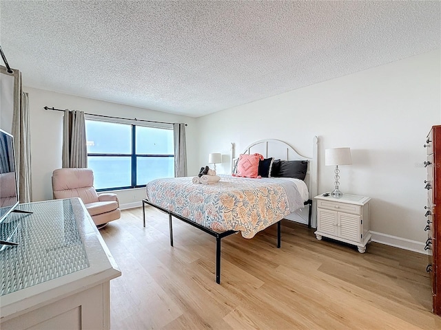 bedroom featuring a textured ceiling, light wood-style flooring, and baseboards