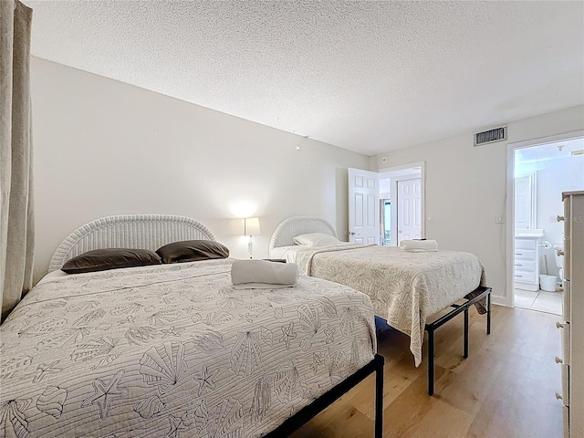 bedroom featuring light wood-style flooring, visible vents, and a textured ceiling