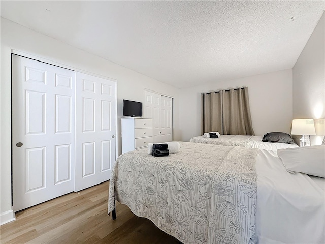 bedroom with light wood-style flooring, a textured ceiling, and multiple closets