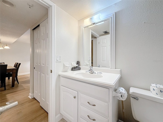 bathroom featuring toilet, wood finished floors, an inviting chandelier, a textured ceiling, and vanity