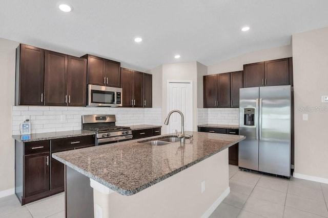 kitchen featuring dark stone counters, stainless steel appliances, dark brown cabinets, and a sink