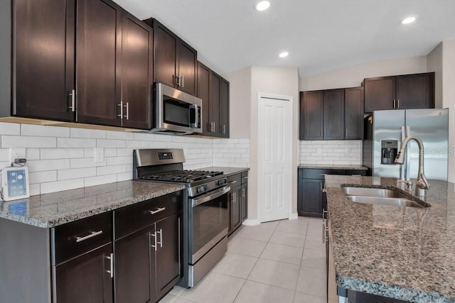 kitchen with dark brown cabinetry, light tile patterned floors, dark stone counters, and stainless steel appliances