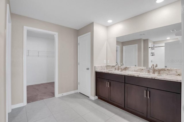 full bath with a sink, baseboards, double vanity, a stall shower, and a walk in closet