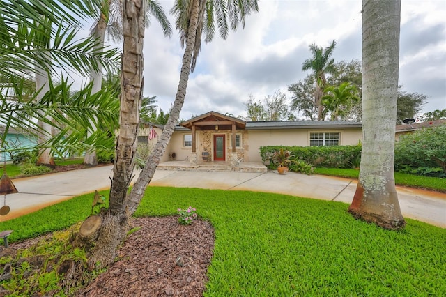 view of front of property featuring stone siding, a front yard, driveway, and stucco siding