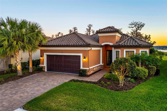 mediterranean / spanish home featuring decorative driveway, a tile roof, stucco siding, a garage, and a front lawn