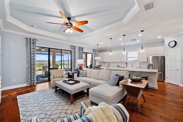 living area featuring dark wood-style floors, a tray ceiling, visible vents, and baseboards