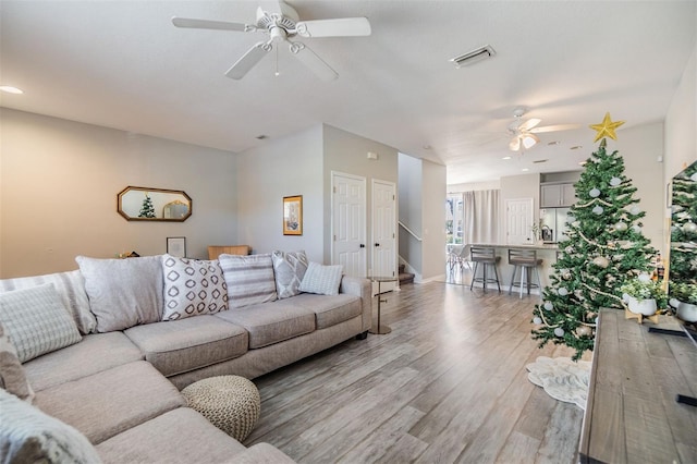 living room with ceiling fan, visible vents, baseboards, stairs, and light wood-style floors