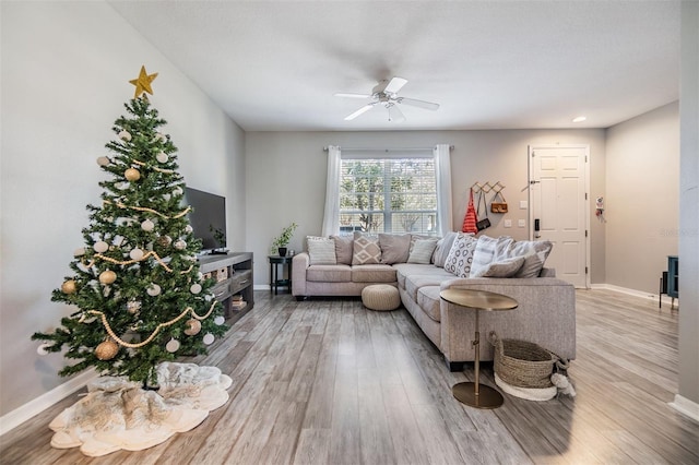 living area with light wood-type flooring, ceiling fan, and baseboards